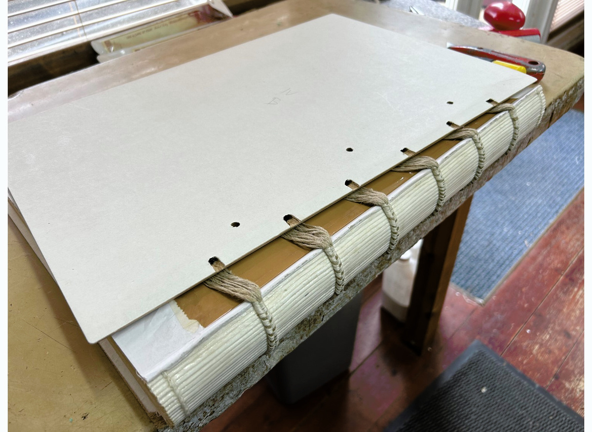 Shows the outside of a board covered with acid free paper and slots cut for lacing