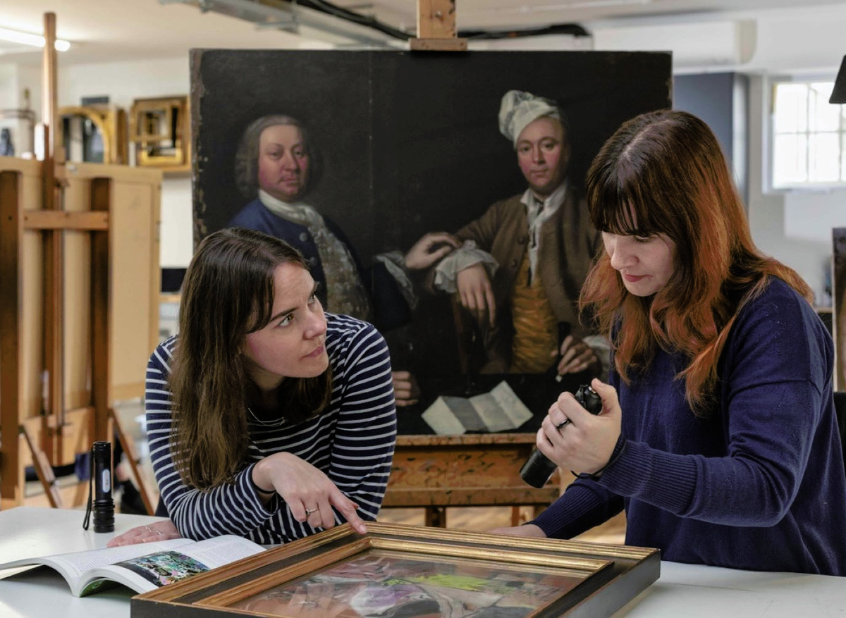 Conservators Emily and Rita collaboratively assessing a painting for treatment
