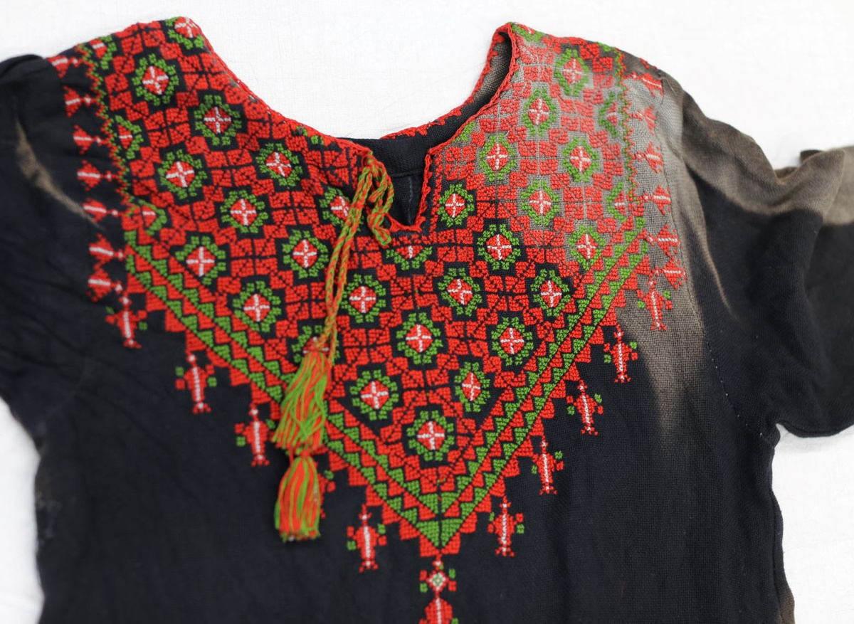A detail of the embroidered chest panel of the child’s dress with bleached marks from exposure